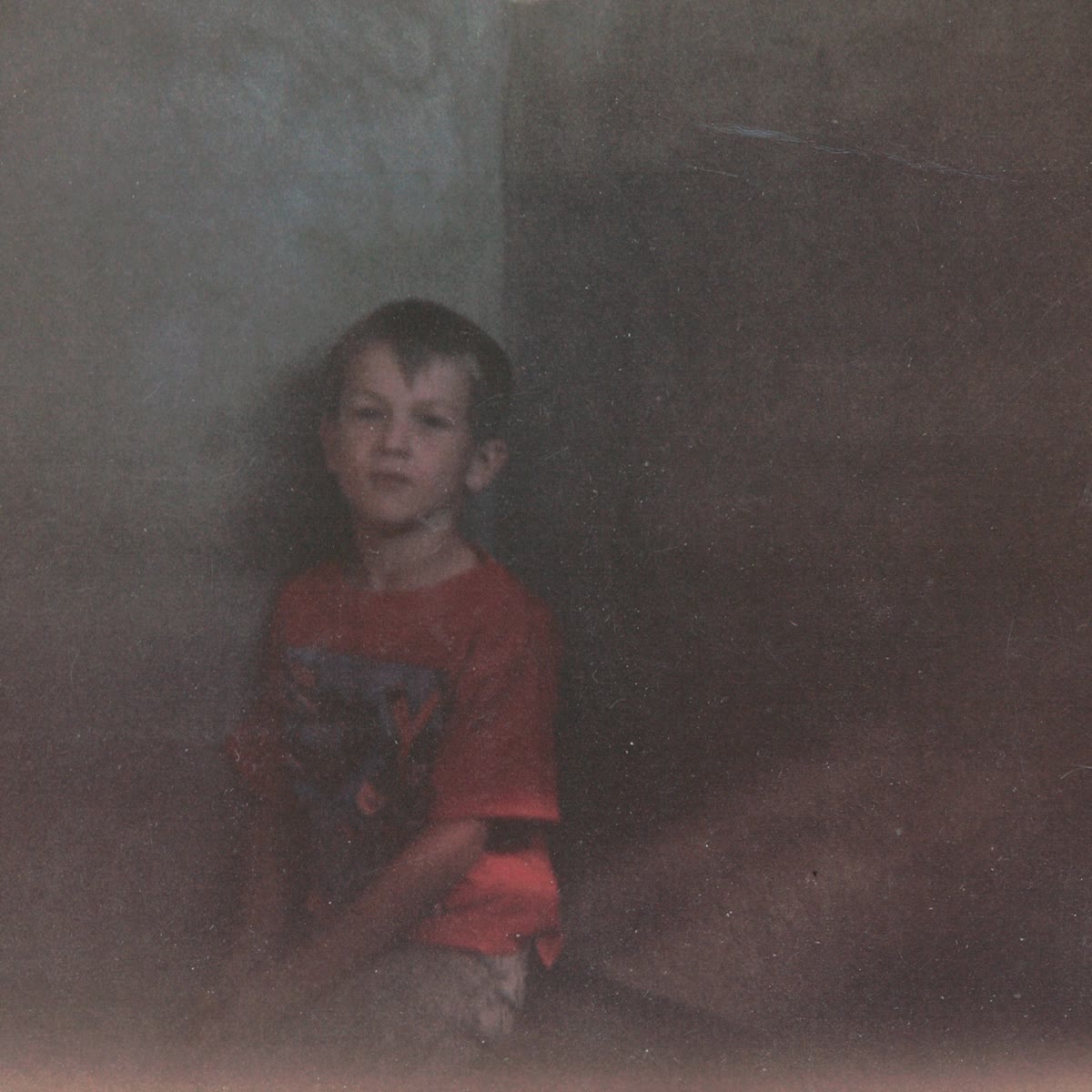 When I Fell Asleep cover art: a faded film photograph of a young boy in a red T-shirt sitting against a wall, looking at the camera
